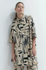 Vestido plisado color beige con estampado abstracto en negro, corte recto, cuello camisero y mangas cortas.