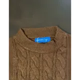 Sweater de punto color blanco marfil, con diseño de trenzas frontales, cuello redondo y mangas largas con puños elásticos acanalados.
