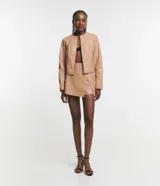 Campera básica de cuero sintético (PU) color marrón oscuro, con cuello redondo, cierre frontal y recortes decorativos. Cuenta con mangas largas y bolsillos con cierre.