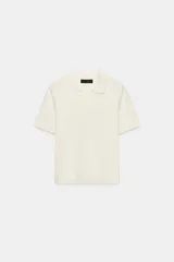 Top de punto color crudo, con cuello polo y escote en V. Cuenta con mangas cortas y detalle de puntilla con forma de onda en el cuello y los puños.