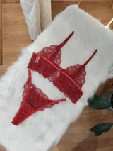 Conjunto de lencería de dos piezas confeccionado en encaje rojo. Incluye un bralette estilo top con breteles regulables y una tanga con laterales ajustables.