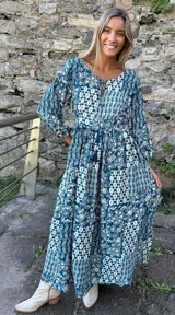Vestido midi de corte holgado con estampado tipo paisley en tonos azul y blanco. Presenta mangas tres cuartos, escote redondo con pequeña abertura frontal y cordón ajustable en la cintura con borlas decorativas.