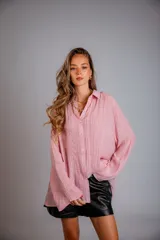 Camisa de manga larga color rosa pálido, con cuello camisero, botones frontales y detalles de encaje o bordado vertical a lo largo de la botonera.