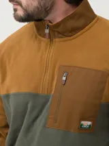 Buzo de polar con diseño color block en tonos tostado y verde oliva. Presenta cuello alto con cierre medio, bolsillo frontal con cierre y parche decorativo con logo de la marca.
