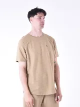 Remera de manga corta con textura de rayas horizontales en relieve, cuello redondo y pequeño aplique metálico en el pecho.