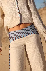 Pantalón de lino de corte ancho y tiro medio, color natural, con detalles de bandas laterales y cintura en estampado rayado azul y marrón.