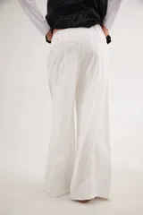 Pantalón de jean con diseño de tiro medio-bajo y piernas anchas. Presenta una pretina ancha con cierre de tres botones metálicos frontales, pinzas decorativas en la cintura y bolsillos delanteros funcionales.