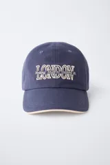 Gorra de béisbol azul marino con visera curva y detalle de borde en color crema. Presenta un bordado frontal con la palabra 'LONDON' en tipografía estilo varsity y texto adicional debajo.