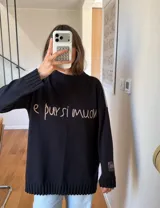 Sweater de punto negro oversize, con cuello redondo y hombros caídos, de manga larga y silueta amplia. Presenta bordado artesanal en el frente con la frase "e pur si muove" y líneas en contraste en los hombros.
