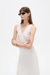 Musculosa de algodón sin mangas, de corte cruzado con cuello en V y diseño holgado, color blanco con estampado de lunares bordó y lazo lateral para ajustar.