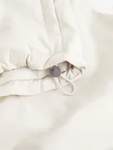 Chaleco blanco hueso acolchado, con cuello alzado de punto de canalé, cierre frontal con cremallera, bolsillos laterales con botón a presión y logo de Calvin Klein en el pecho.