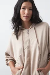 Campera con capucha y cierre frontal, de silueta relajada, hombros caídos y bolsillos laterales. Presenta terminaciones elastizadas en puños y ruedo, con líneas de recorte frontales y cierre metálico con tirador circular.