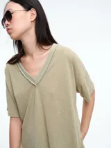 Remera de corte holgado y silueta cómoda, con escote en V y mangas cortas. Presenta costuras visibles en el cuello y los hombros, con un diseño minimalista y versátil.