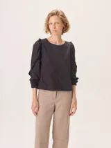 Camisa blanca de manga larga con volados en los hombros y puños ajustados con elástico. El cuerpo es de tejido de punto y las mangas y el delantero son de tejido de camisa.