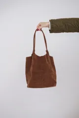 Bolso tote de gamuza color marrón con doble asa de hombro y broche metálico de cierre. Incluye un neceser pequeño.