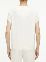 Blusa blanca de poliéster reciclado con cuello redondo, mangas cortas y cierre con cremallera en la espalda. Presenta una abertura en la parte delantera con barra metálica.