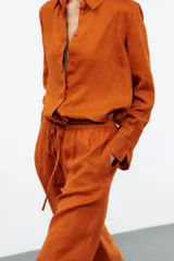 Camisa color coral confeccionada en lino 100%, de corte recto, con cuello solapa, manga larga con puños abotonados y cierre frontal con botones.