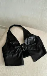Top de cuero sintético negro con escote profundo en V, estilo halter y cierre frontal mediante una hebilla metálica ajustable.