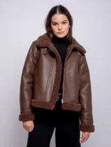 Campera marrón de símil cuero con interior de corderito, cierre cruzado con cremallera, hebilla metálica en el cuello y dos bolsillos laterales.