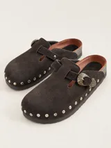 Zueco de gamuza marrón oscuro, forrado en cuero vacuno, con tira ajustable con hebilla metálica decorativa y tachas plateadas alrededor de la suela.