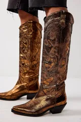 Bota alta estilo cowboy color dorado metalizado, con bordados decorativos y puntera en punta.