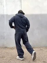 Conjunto de dos piezas compuesto por un buzo con capucha y cierre frontal y un pantalón de jogging, ambos confeccionados en tejido con efecto acid wash en color gris oscuro. El buzo cuenta con bolsillos frontales y logo bordado, mientras que el pantalón presenta un corte holgado y logo bordado en la pierna.