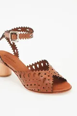 Sandalia de cuero vacuno color suela con diseño calado en la capellada y en la tira del tobillo. Presenta un taco bloque de madera y cierre con hebilla metálica.