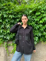 Camisa negra de tejido fino con detalles de cuero en los bolsillos y corte holgado.