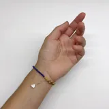 Pulsera elaborada con mini cuentas facetadas de Lapislázuli y tres Perlas de Río en el centro. Las terminaciones son en acero con baño de oro y cuenta con un dije de nácar.