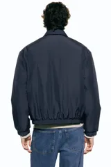 Campera de estilo coach, color azul marino, con cuello inglés, cierre frontal con botones a presión y bolsillos laterales insertados. Presenta puños y bajo con elástico, y cuenta con forro interior acolchado.