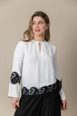 Blusa color marfil de seda con incrustaciones de cruni negro, mangas amplias y cuello cerrado con abertura.