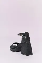 Sandalias de cuero negro con plataforma y tacón cuadrado alto. Presentan una tira delgada sobre los dedos y pulsera tobillera con hebilla dorada.