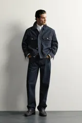 Campera de denim azul oscuro de corte cropped, con cuello camisero, bolsillos delanteros con solapa y cierre frontal oculto con botones metálicos.