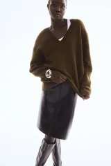 Sweater de punto suave color verde oliva, con cuello en V, hombros caídos y remates acanalados en puños y bajo.