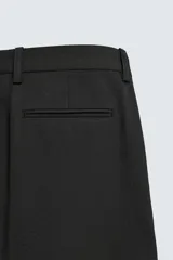 Pantalón straight fit color negro confeccionado en tejido con lana, con detalle de pliegues en el delantero, bolsillos frontales y traseros, y cierre frontal con cremallera y botón.
