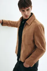 Campera de gamuza color camel, con cuello camisero, cierre frontal y bolsillos laterales con cierre. Presenta un corte estándar y forro interior.