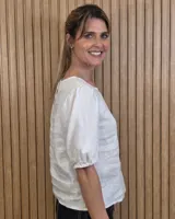 Blusa blanca de lino, con cuello redondo y mangas cortas abullonadas con frunces en los hombros.