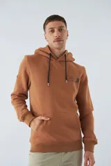 Buzo de algodón color marrón con capucha, bolsillo tipo canguro, mangas largas y logo estampado en el pecho.