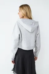 Campera tipo hoodie de corte cropped, color gris melange, con cierre frontal de cremallera, capucha ajustable con cordones y bolsillos tipo canguro.