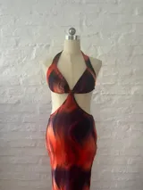 Vestido largo con estampado abstracto en tonos naranja y azul, con escote halter y aberturas laterales en la cintura.