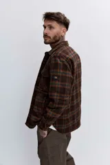 Campera tipo sobrecamisa de franela a cuadros en tonos marrones y verdes, con cuello clásico, cierre frontal de botones y bolsillos con solapa en el pecho.