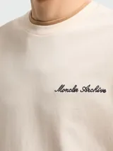 Remera de algodón color beige con cuello redondo, manga corta y bordado con la inscripción "Moncler Archive" en el pecho. Presenta un parche con el logo de la marca en la manga izquierda.