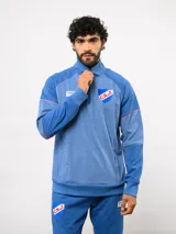 Buzo deportivo de medio cierre marca Umbro del Club Nacional de Football. Presenta un diseño en tonos azul y gris jaspeado, con cuello alto, mangas largas y detalles de costuras en contraste. Incluye el escudo del club y logo de la marca en el pecho.