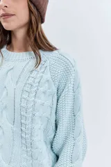 Sweater de punto en color celeste, con diseño de trenzas y textura en relieve. Presenta cuello redondo, mangas largas con puños ajustados y un corte holgado.