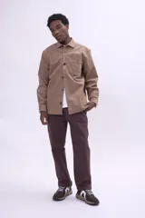 Camisa de pana color tostado, de corte recto y manga larga, con cierre frontal de botones y bolsillo en el pecho.