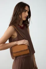 Cartera de hombro pequeña de cuero color tostado con detalles de bordado artesanal y costuras en tono chocolate en los bordes y la solapa. Cuenta con correa larga ajustable.