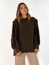 Sweater de punto color negro, con cuello redondo, mangas largas abullonadas y detalles de flecos en las costuras de los hombros y mangas.