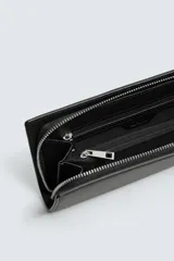 Cartera tipo bandolera de color negro con acabado texturizado. Cuenta con un compartimento principal con cierre de cremallera, interior con dos compartimentos adicionales y asa de hombro ajustable y extraíble.