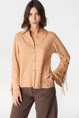 Camisa de color camel con textura geométrica en relieve, cuello clásico y cierre frontal con botones. Presenta mangas largas con detalle de tiras ajustables y aberturas en los puños.
