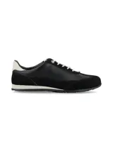 Zapatilla deportiva de mujer, estilo retro running, en tonos negro y blanco. Presenta una combinación de materiales, incluyendo cuero liso negro en el cuerpo principal, gamuza negra en la puntera y talón, y un detalle de cuero blanco en el contrafuerte del talón. Cordones blancos y suela bicolor (blanco y negro).